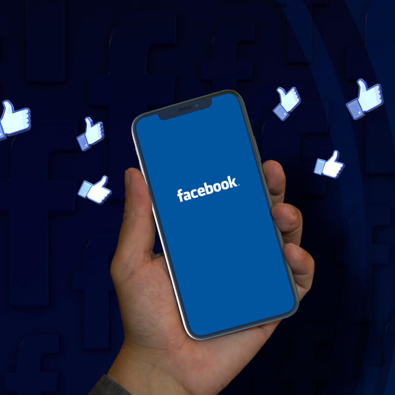 Telefon z logo Facebooka na ekranie trzymany w dłoni z ikonami polubień dookoła