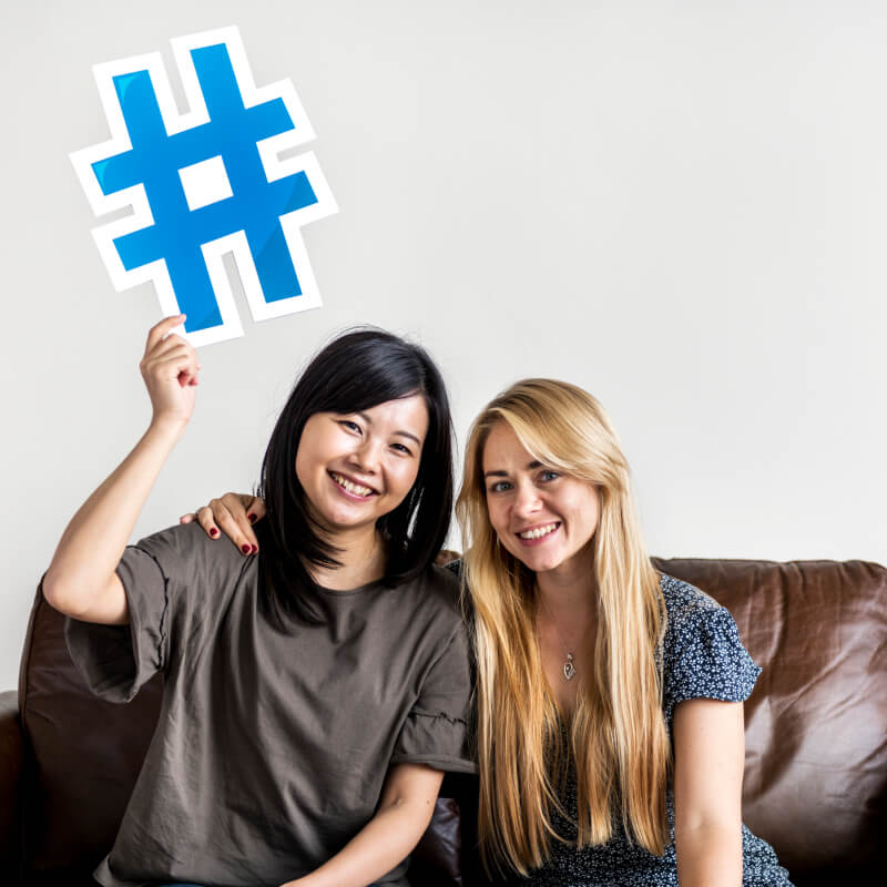 Dwie osoby siedzące na kanapie z symbolem hashtag w dłoni